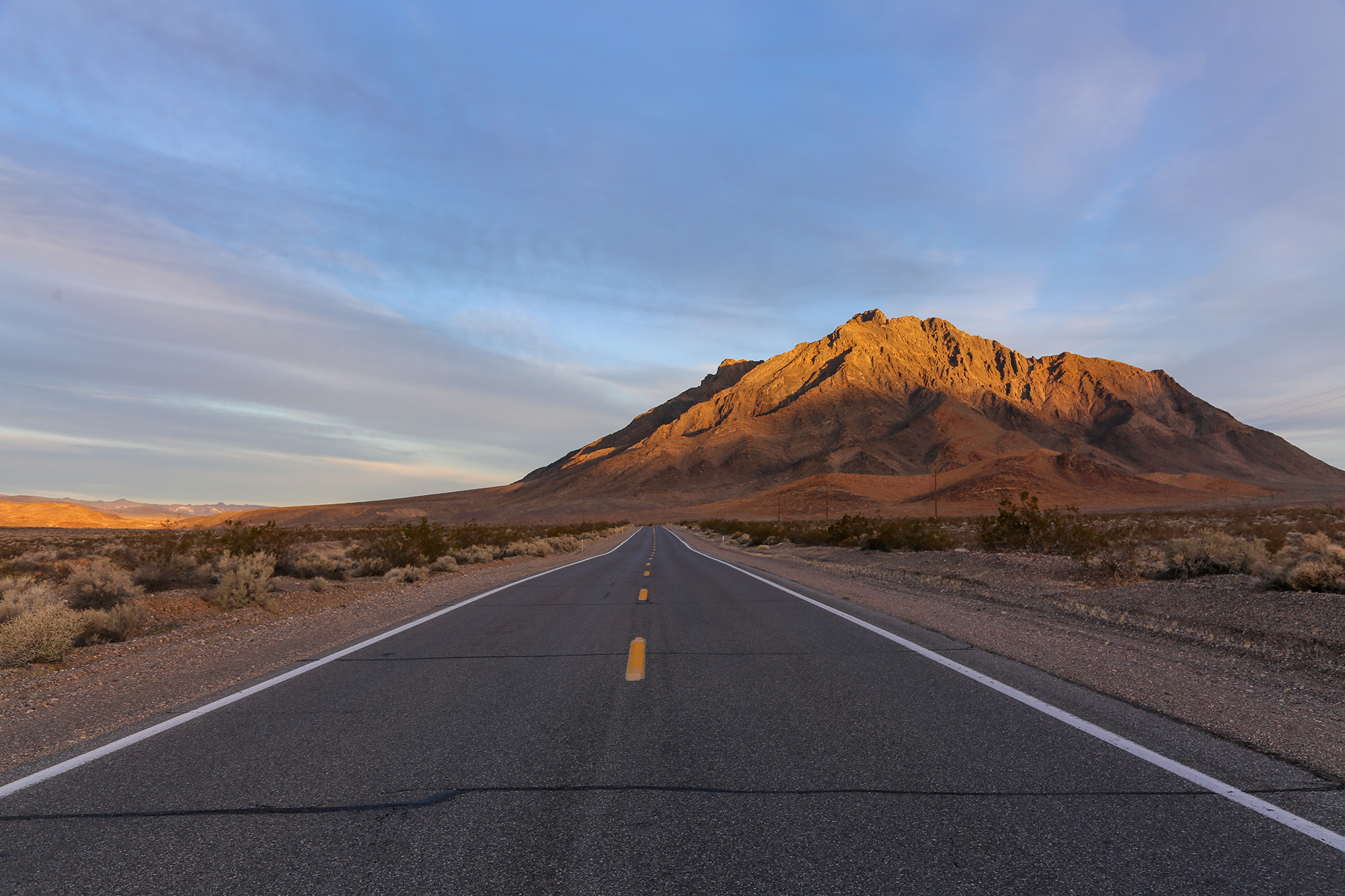 A two lane paved road at sunset near Death Valley Junction in Death Valley National Park, California.