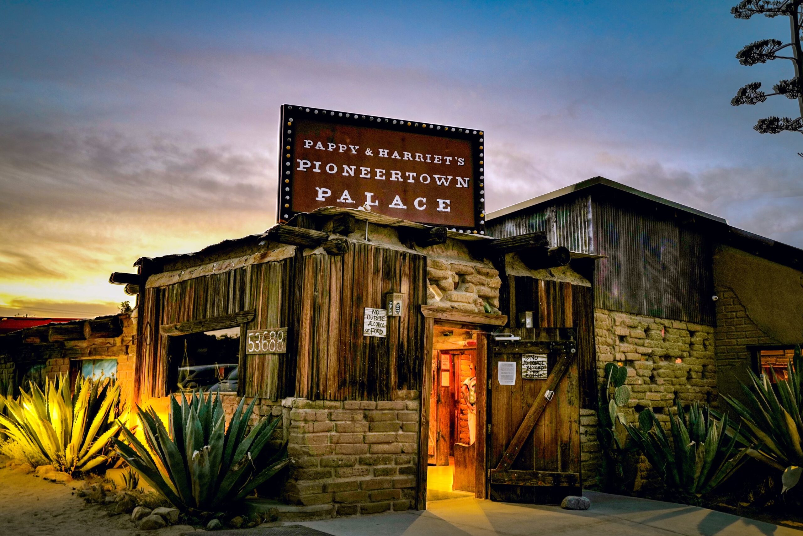 Exterior sunset view of the entrance and sign for Pappy & Harriet's Pioneertown Palace in Pioneertown, California.
