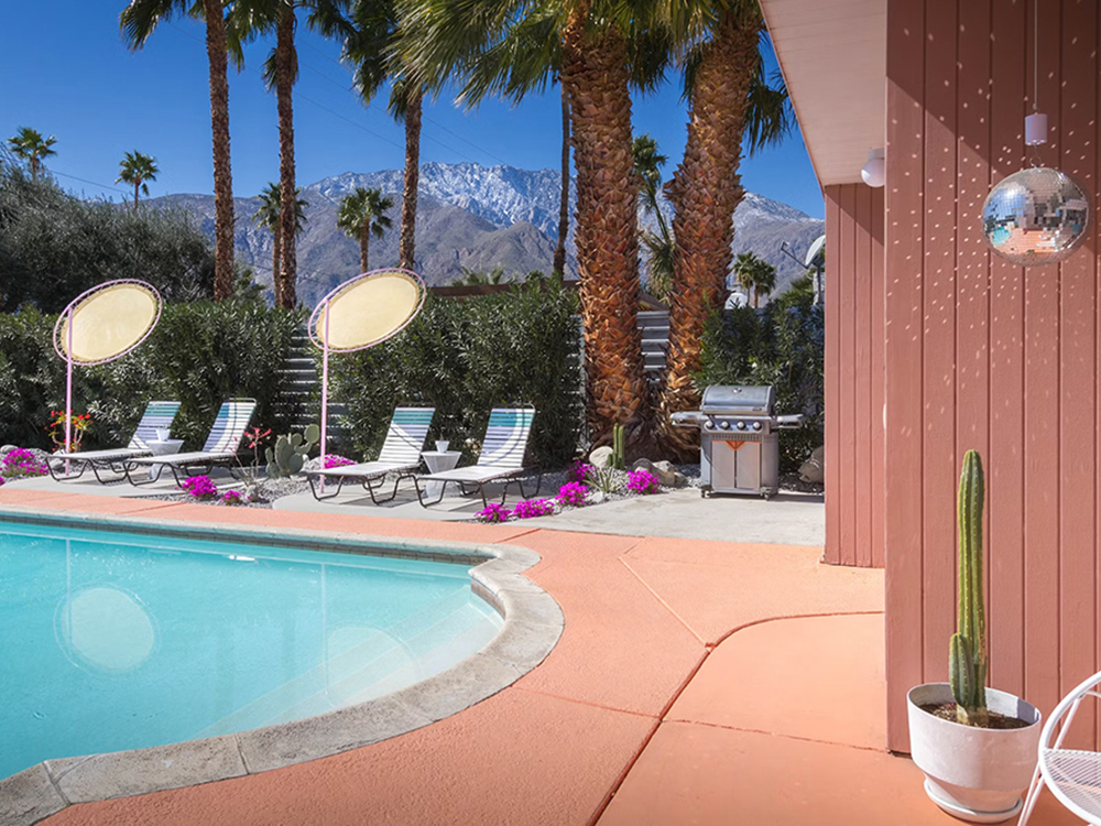 Exterior photo of pink walls with a disco ball, pool, and lounger chairs at Desert Dreamer vacation home in Palm Springs, California
