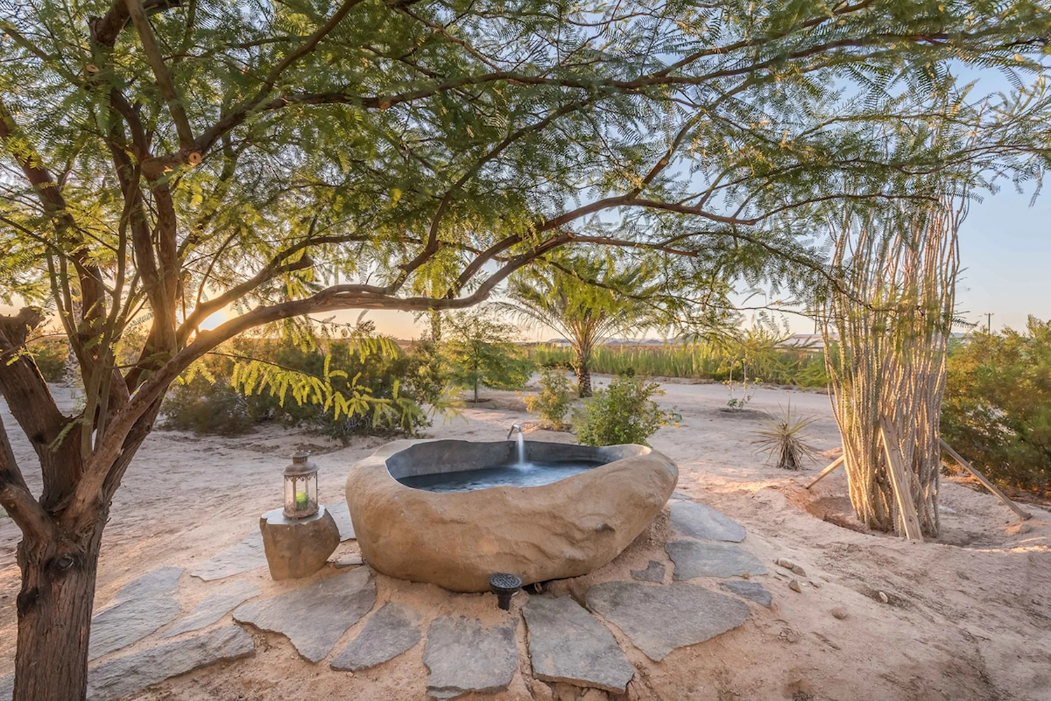 Outdoor hot springs tub with stone patio tiles and surrounded by desert vegetation at the Ocotillo Oasis in Wonder Valley, California.