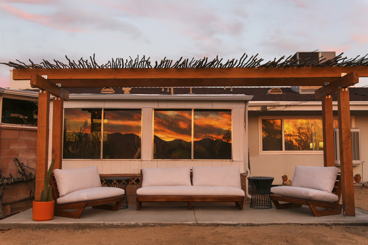 Sunset view of the backyard pergola with the sunset reflected in the home's windows at Las Palmas vacation rental in Yucca Valley, California.