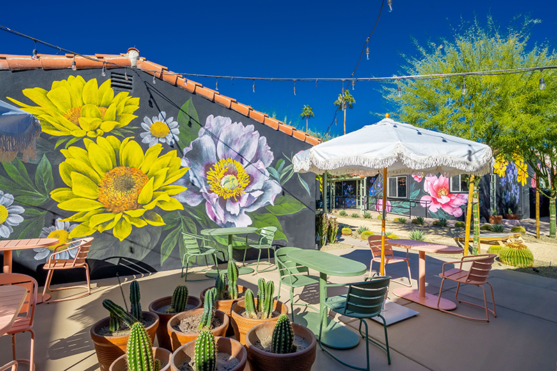 Outside patio seating set against large floral murals at Fleure Noire Hotel in Palm Springs, California.
