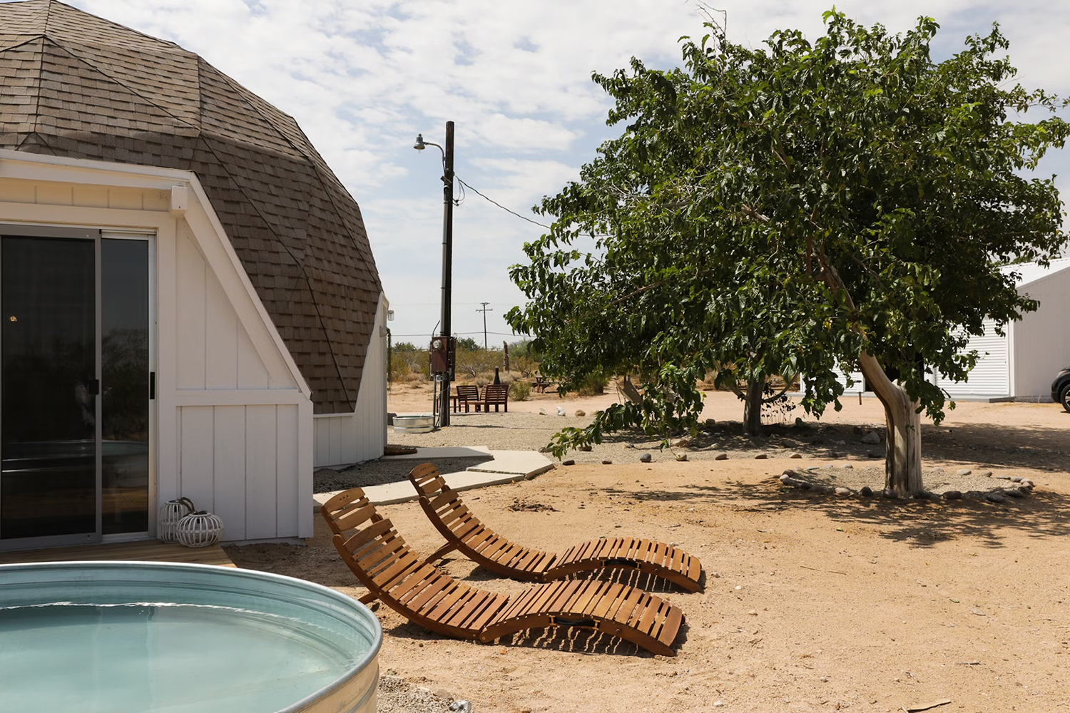 Exterior view of a cowboy pool and two wooden sun lounge chairs at geodesic Joshua Tree vacation rental Abracadabra Dome.