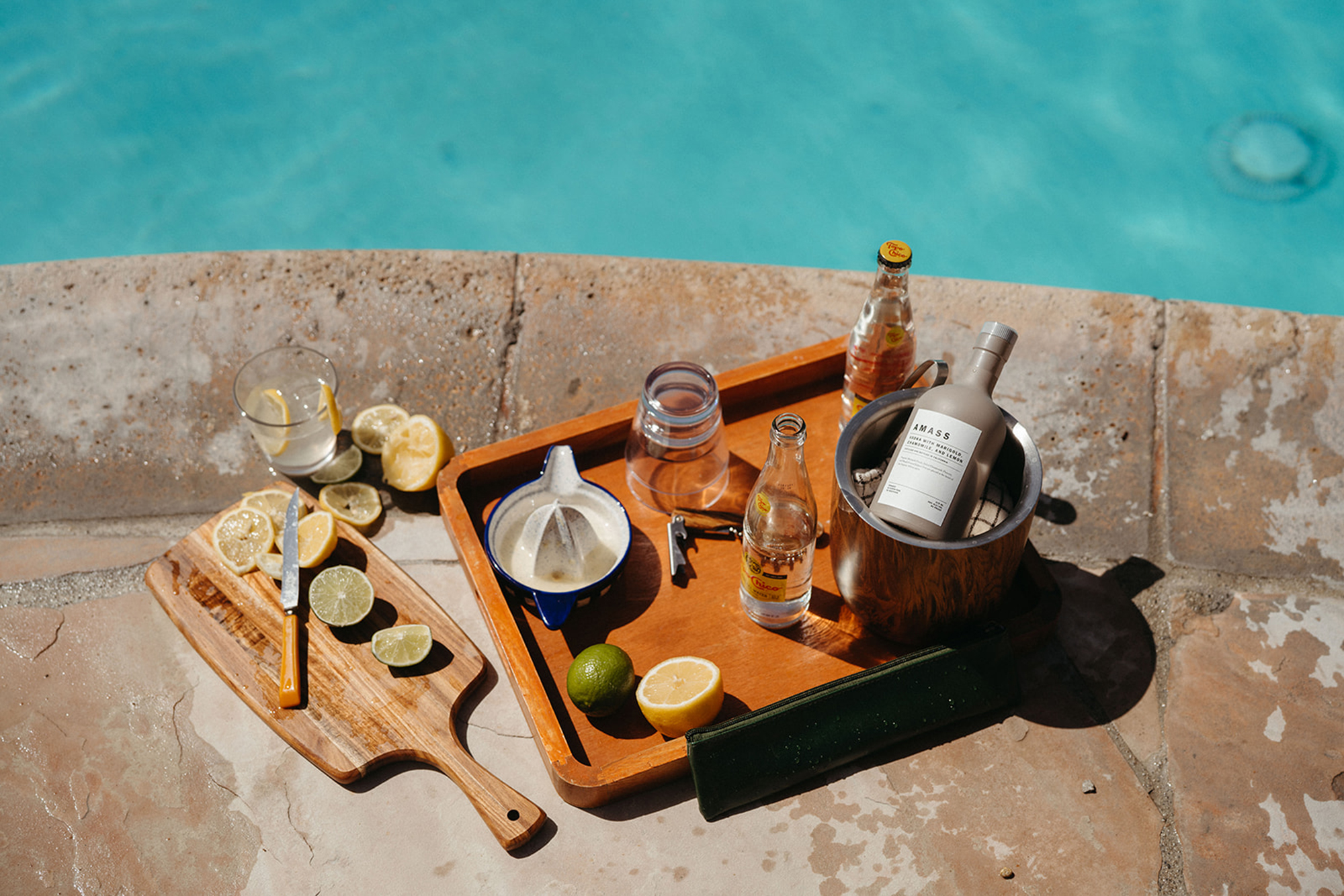 Cocktail Kit with AMASS, Topo Chico, and fresh citrus on a wooden serving tray and cutting board poolside at Casa Cody, Palm Springs.