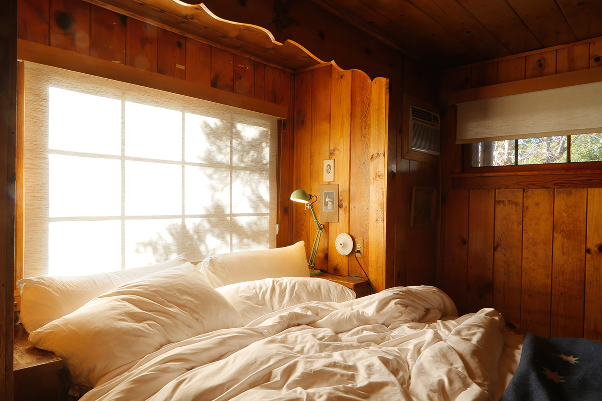 A bed set against a large window in a cozy wood paneled room at the Fireside Inn in Idyllwild, California.