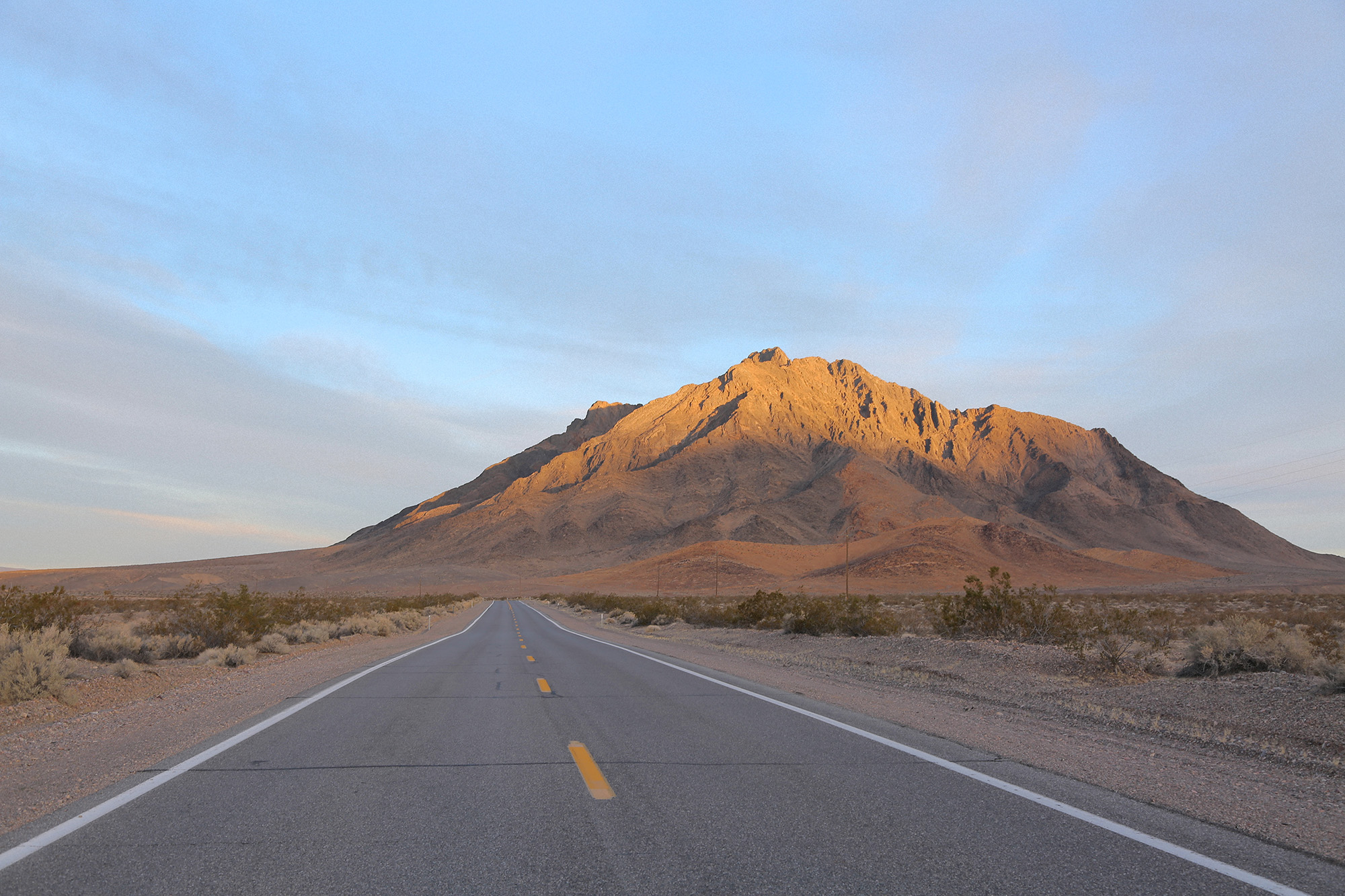A paved road leading to a desert mountain at sunrise in Death Valley National Park.