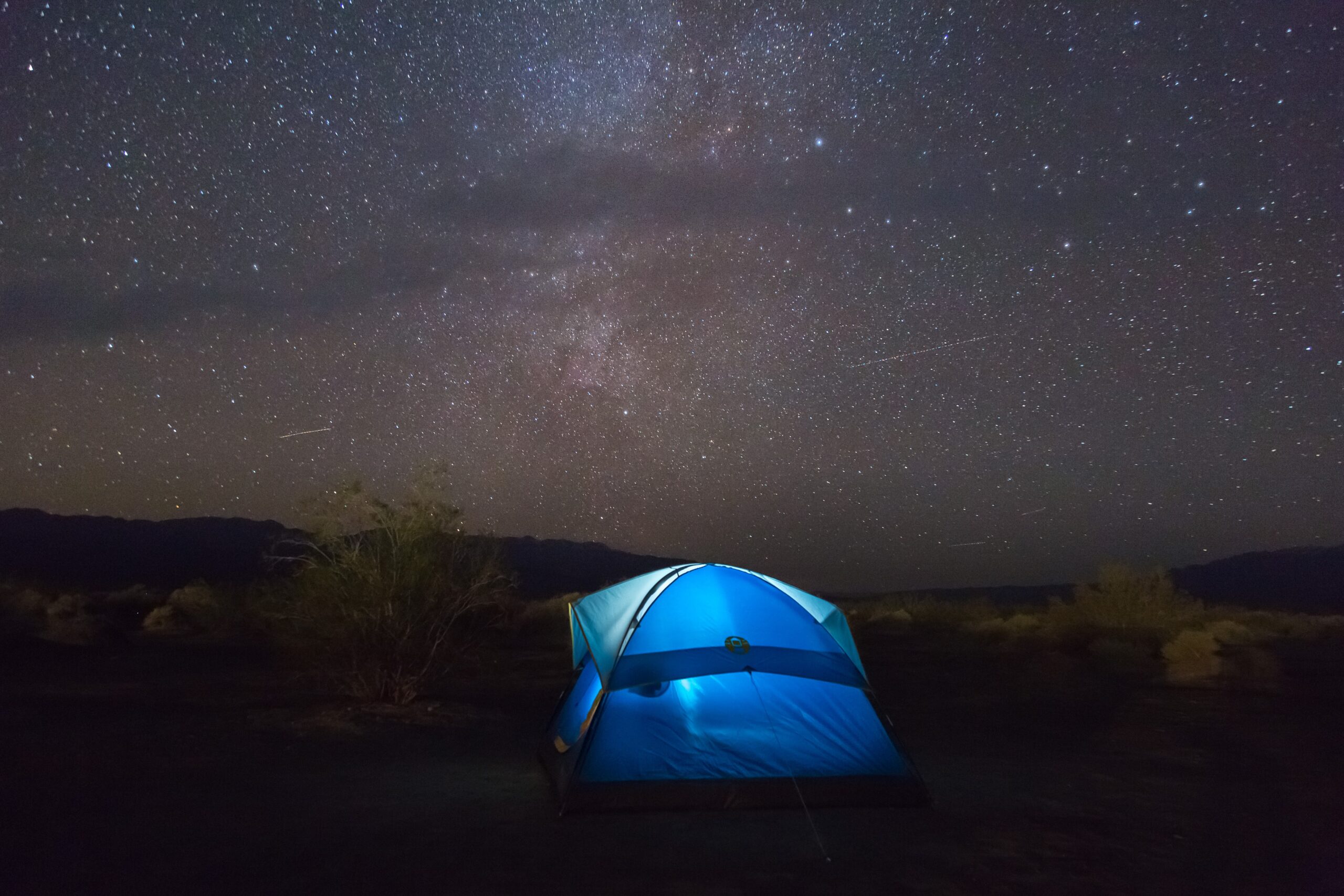 A blue tent illuminated from the interior at night with a starry sky in Death Valley National Park, California. Photo: Wilson Ye.