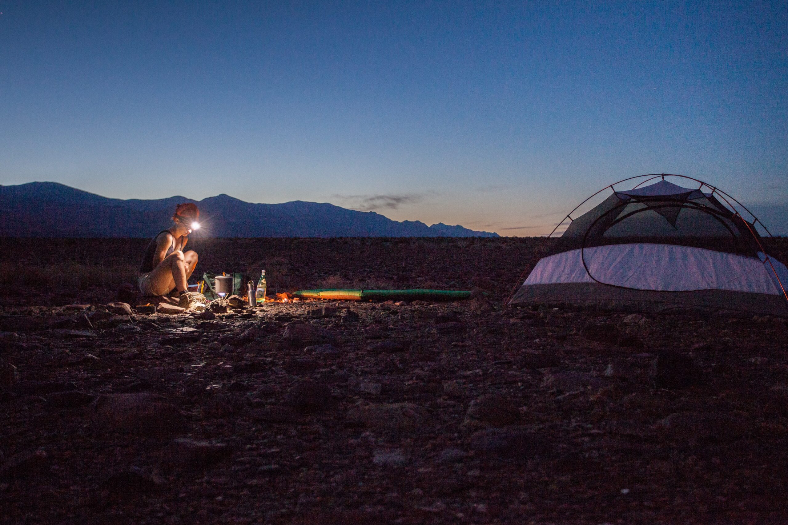 A woman wearing a headlamp and cooking at a campsite at dusk. Photo: Yuriy Rzhemovskiy.