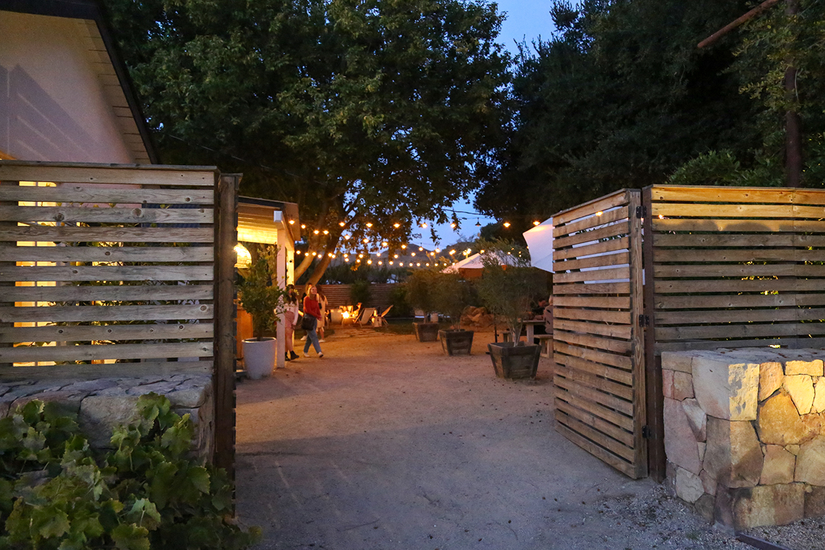 Dusk view of the open gate leading to the patio light lit outdoor seating area at Bodega wine shop in Los Alamos, California.