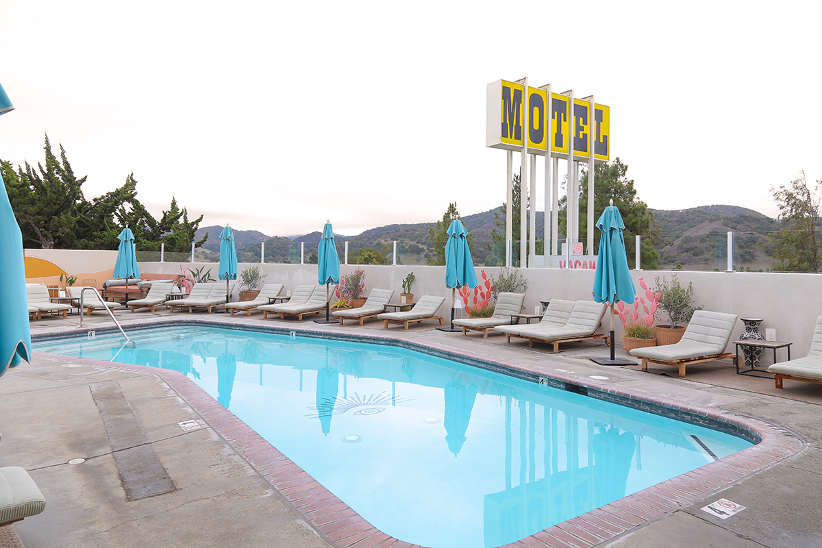The small pool with loungers and umbrellas with a large yellow 'Motel' sign in the backdrop at Skyview Los Alamos.