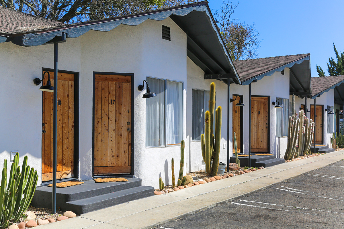 White exterior with black trim and wooden doors at the Alamo Motel in Los Alamos, California.