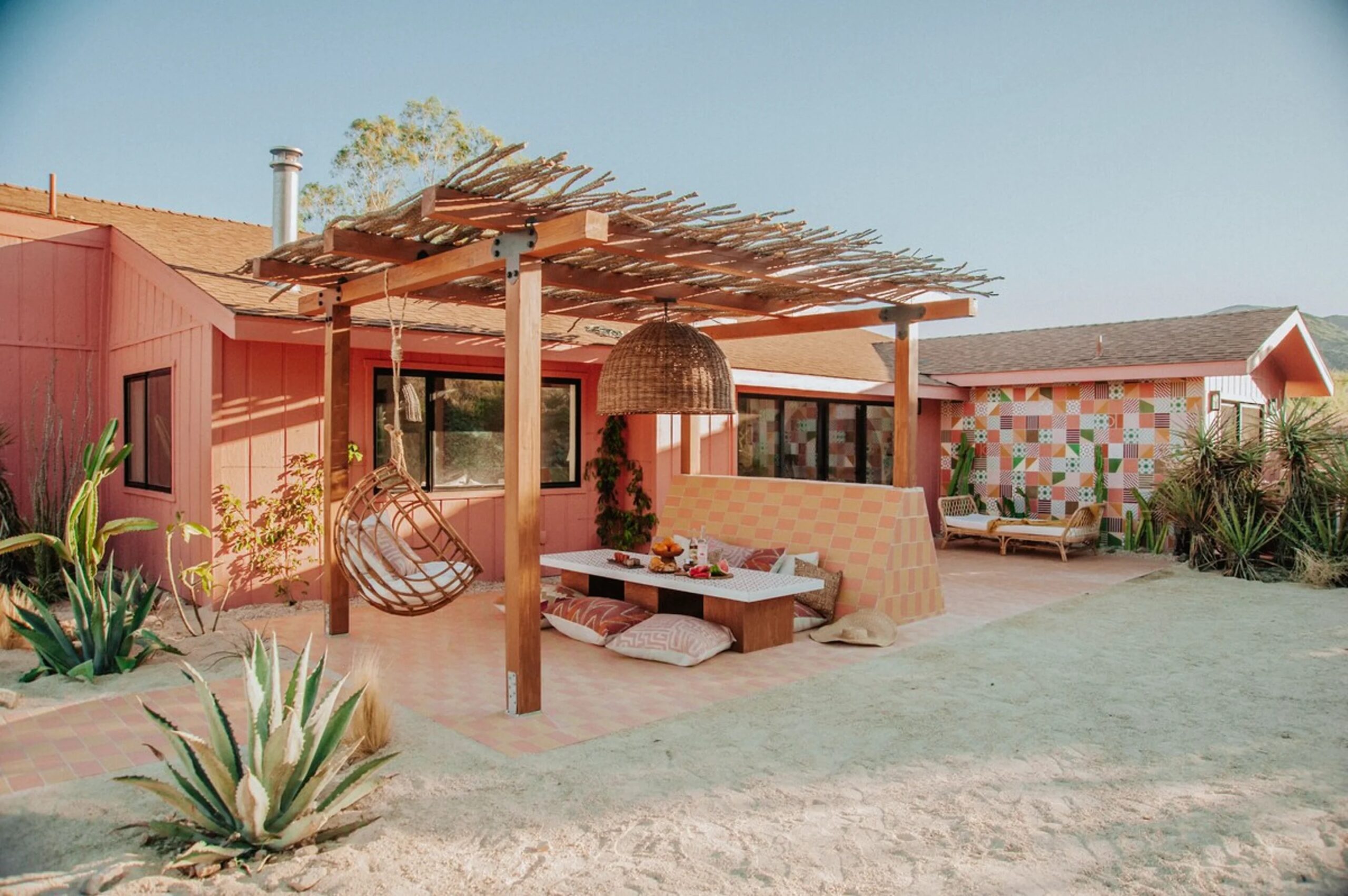 Exterior view of a pergola and dining or lounging spaces at pastel toned Desierto Occidental vacation rental home near Joshua Tree National Park, California.