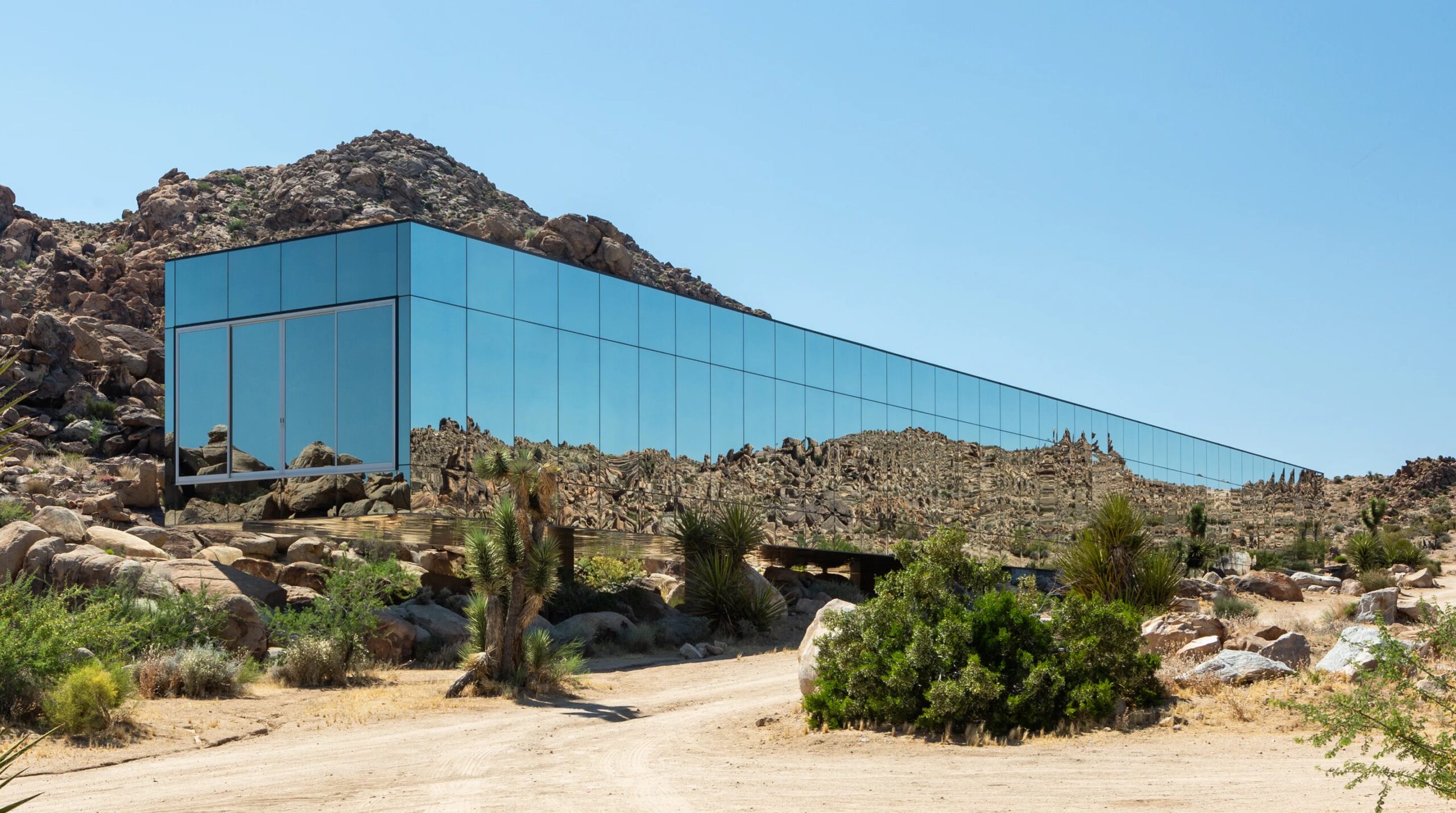 Exterior view of a long mirrored vacation rental home called Invisible House set in the desert near Joshua Tree National Park, California.