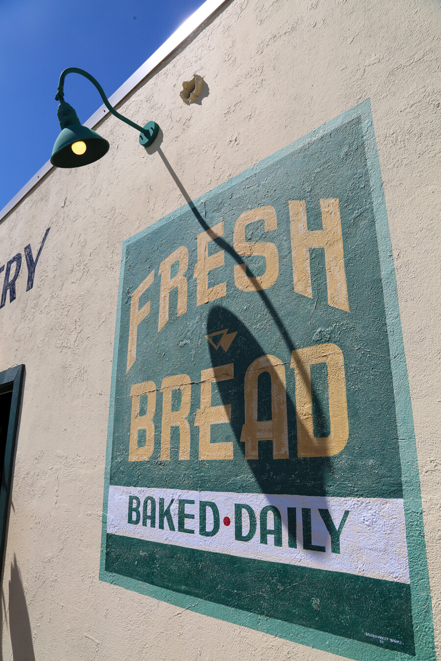 Exterior painted sign that reads 'Fresh bread baked daily' at Bob's Bakery in Los Alamos, California.
