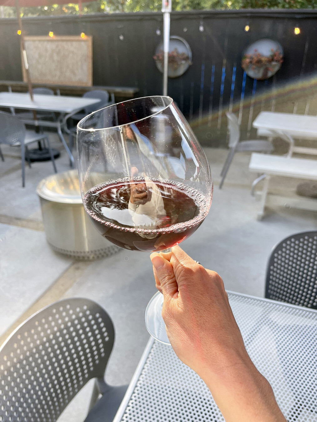 A hand holding a glass of red wine on the patio at Casa Dumetz Wines in Los Alamos, California.