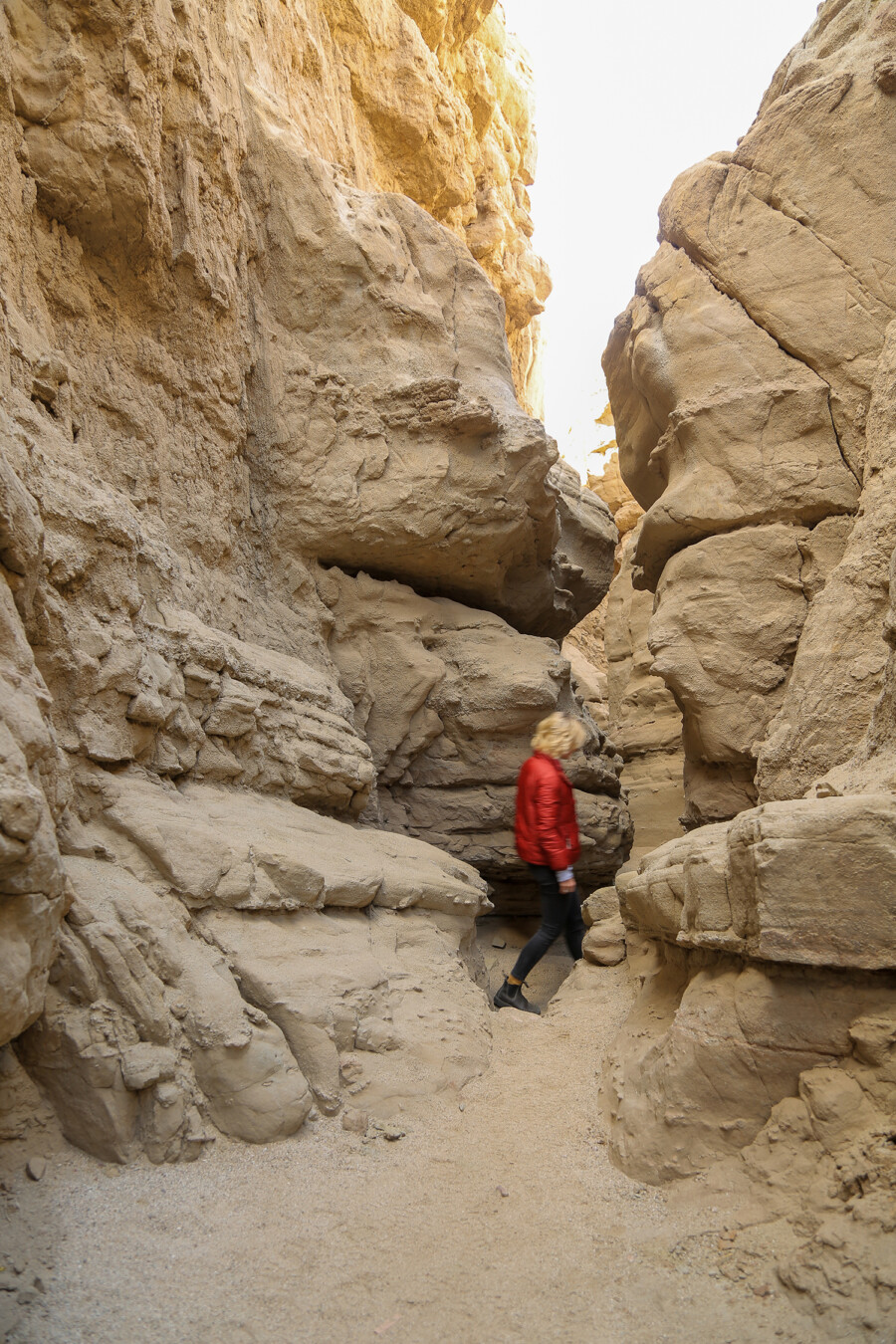 View of a woman hiking through a narrow rocky passageway at Slot Trail in Anza Borrego Desert State Park, California.