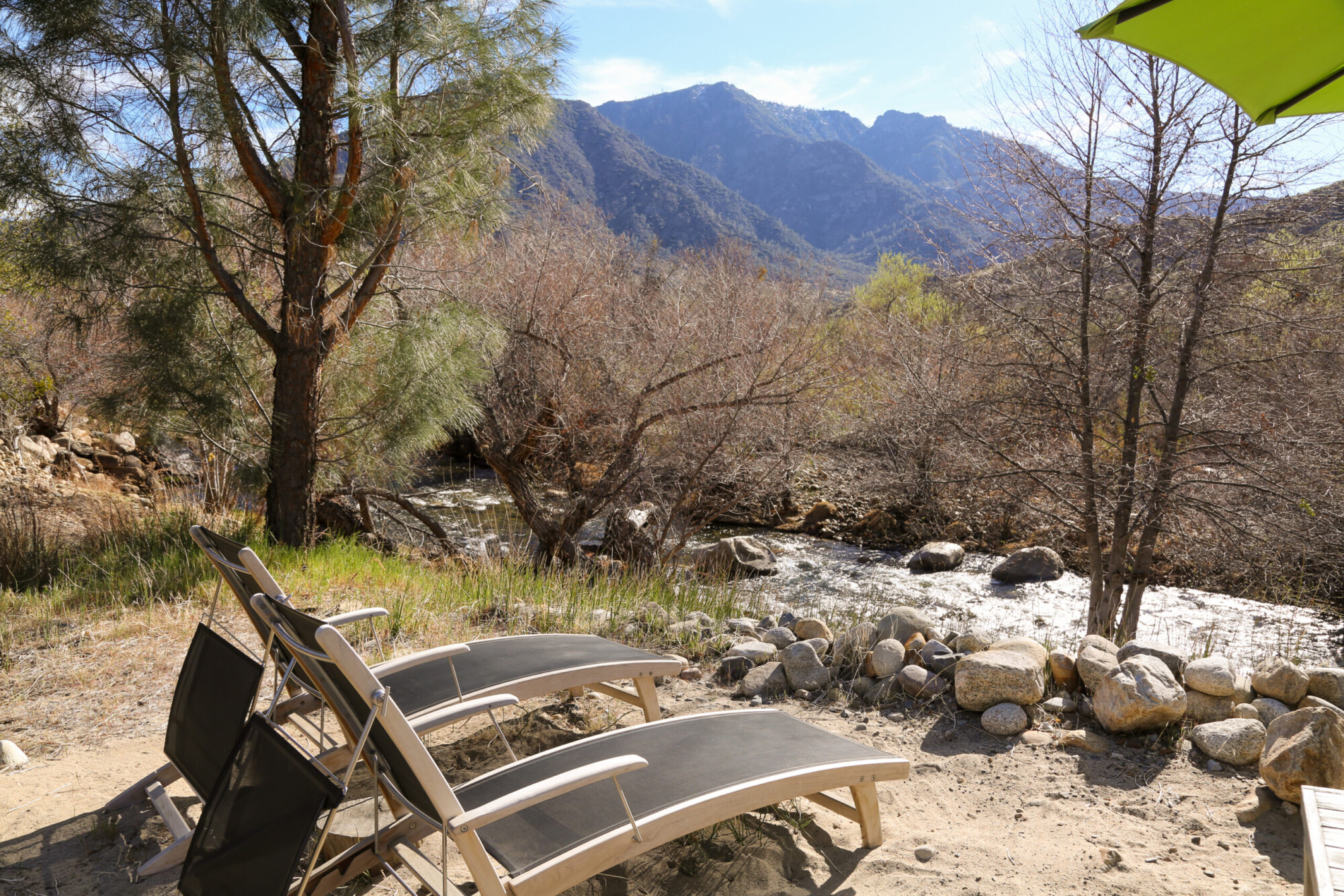 View of two outdoor lounge chairs overlooking a river and the mountain view at Kern River House's River Willow Cabin in Kernville, California.