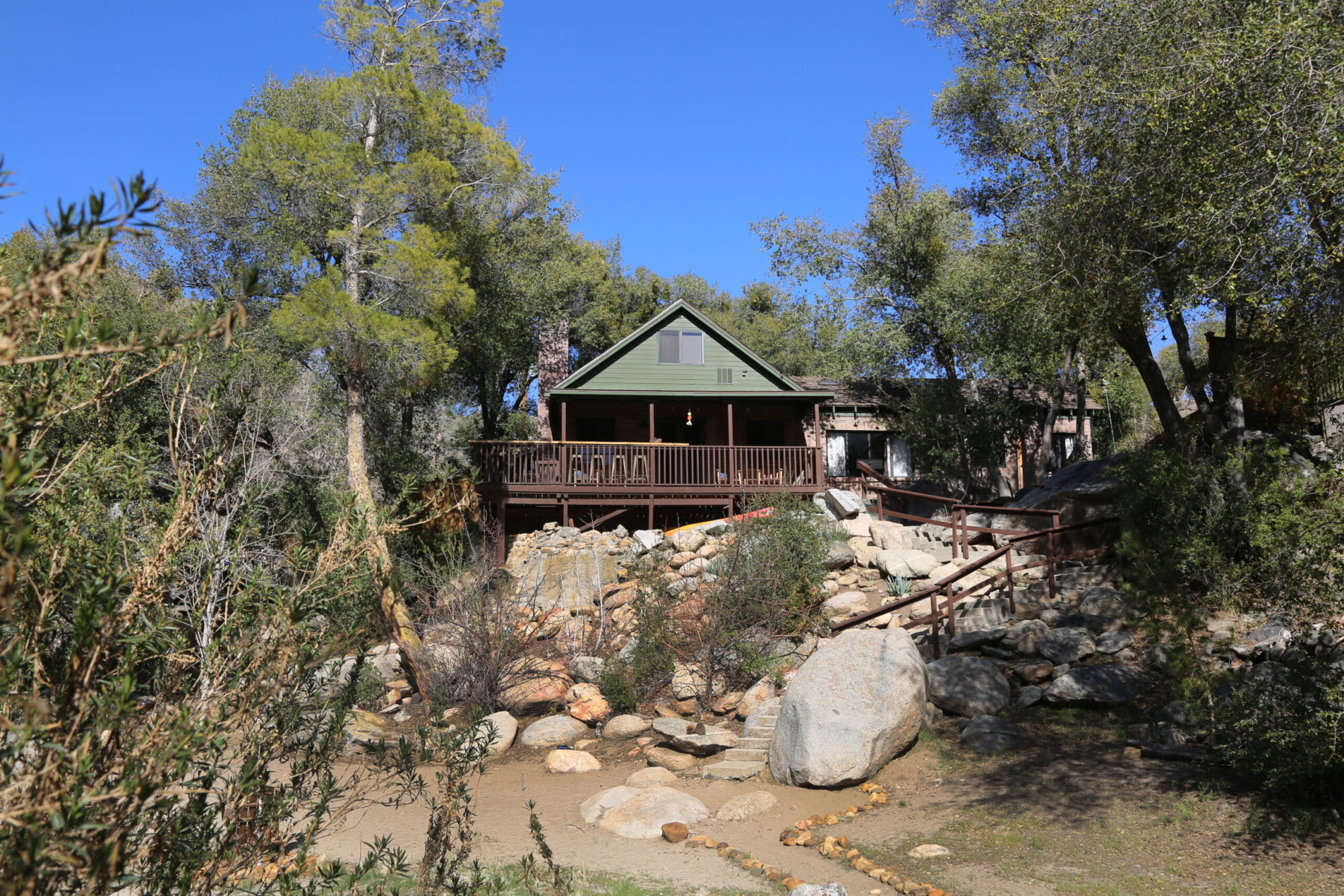 Exterior view of Kern River vacation rental house with a large deck set in surrounding forest near Kernville, California.