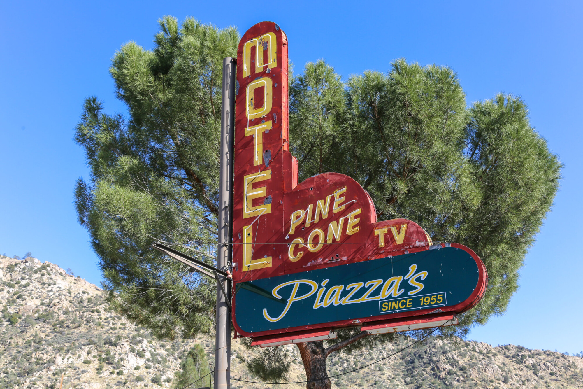 Photo of the the road sign set against a lone tree at a motel called Piazza's Pine Cone Inn in Kernville, California.