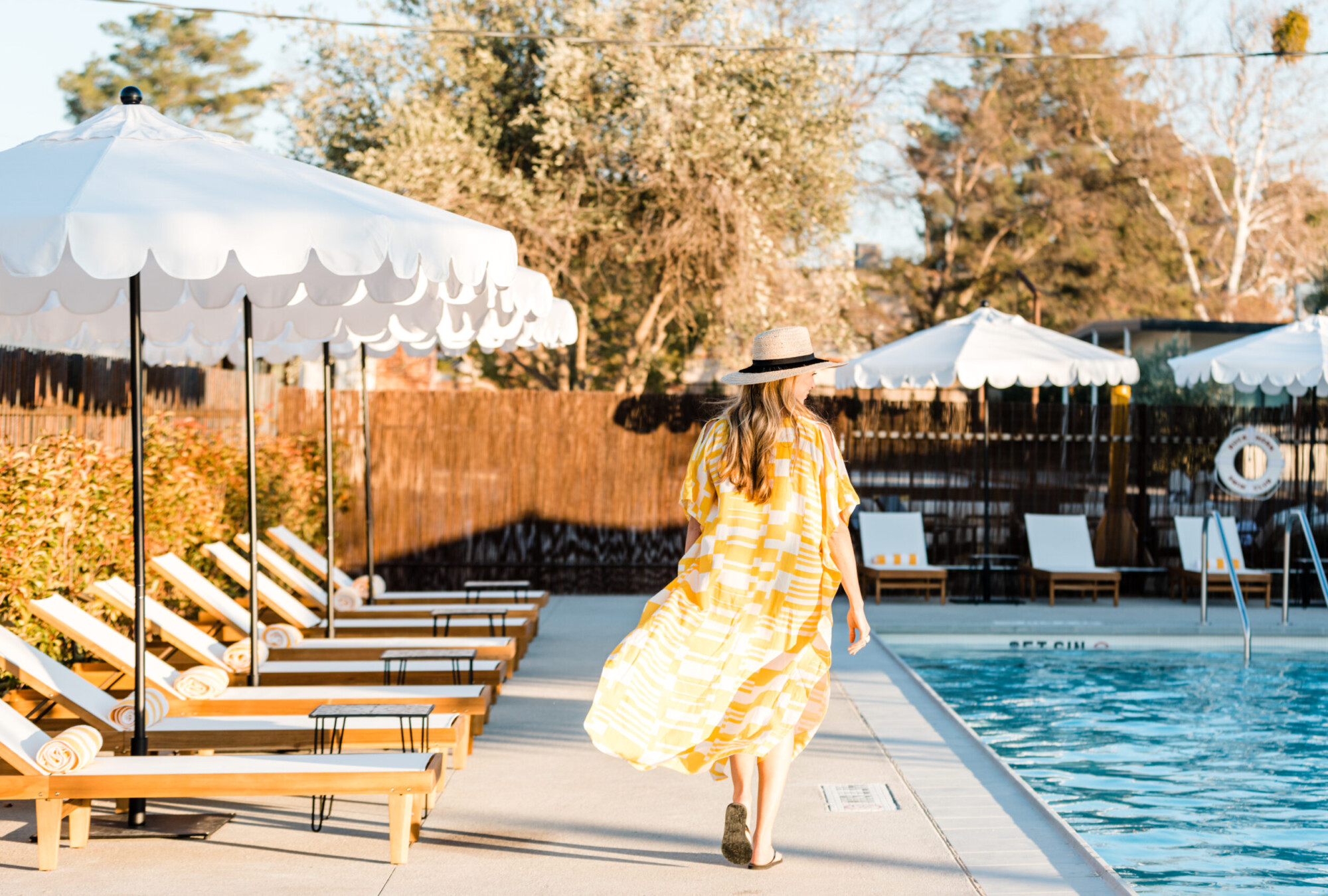 View of a woman walking next to pool loungers and white shade umbrellas a the Cuyama Buckhorn's pool in New Cuyama, California.