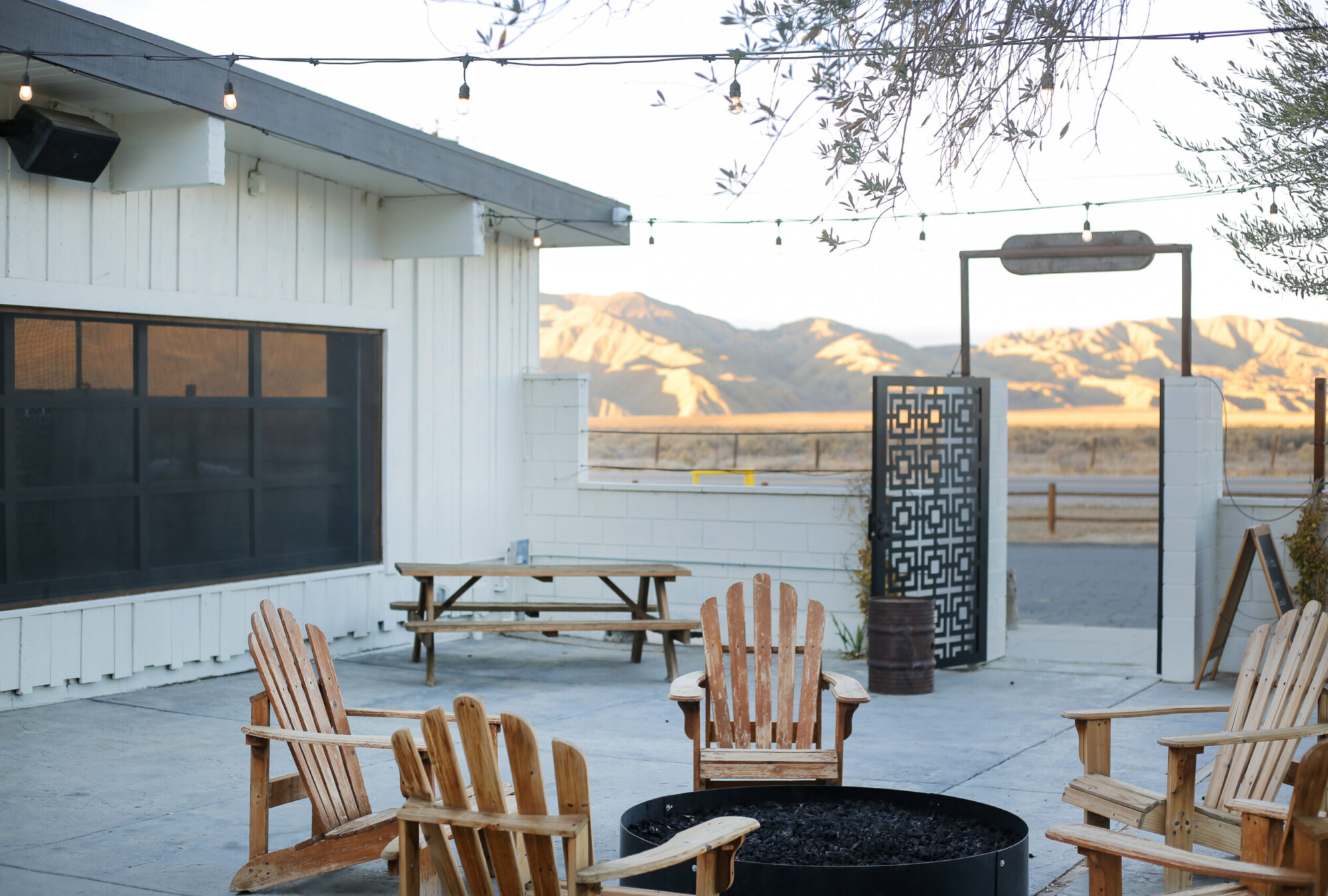 View of the outdoor courtyard with Adirondack chairs and a fire pit with the mountain view in the backdrop at Cuyama Buckhorn in New Cuyama, California.