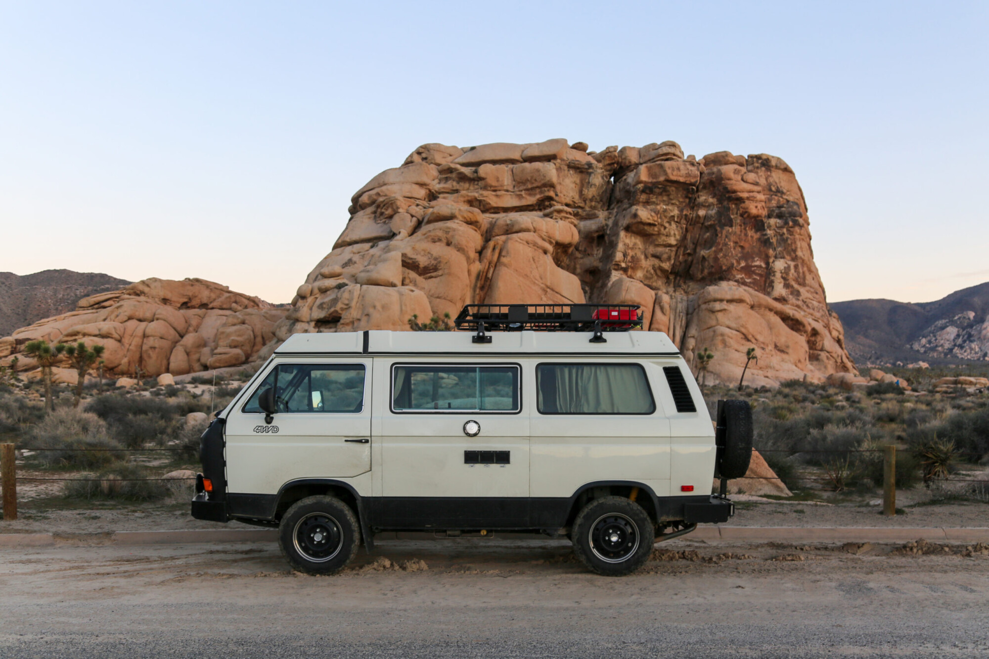 A beige adventure van parked in front of a boulder formation in Joshua Tree National Park, California.
