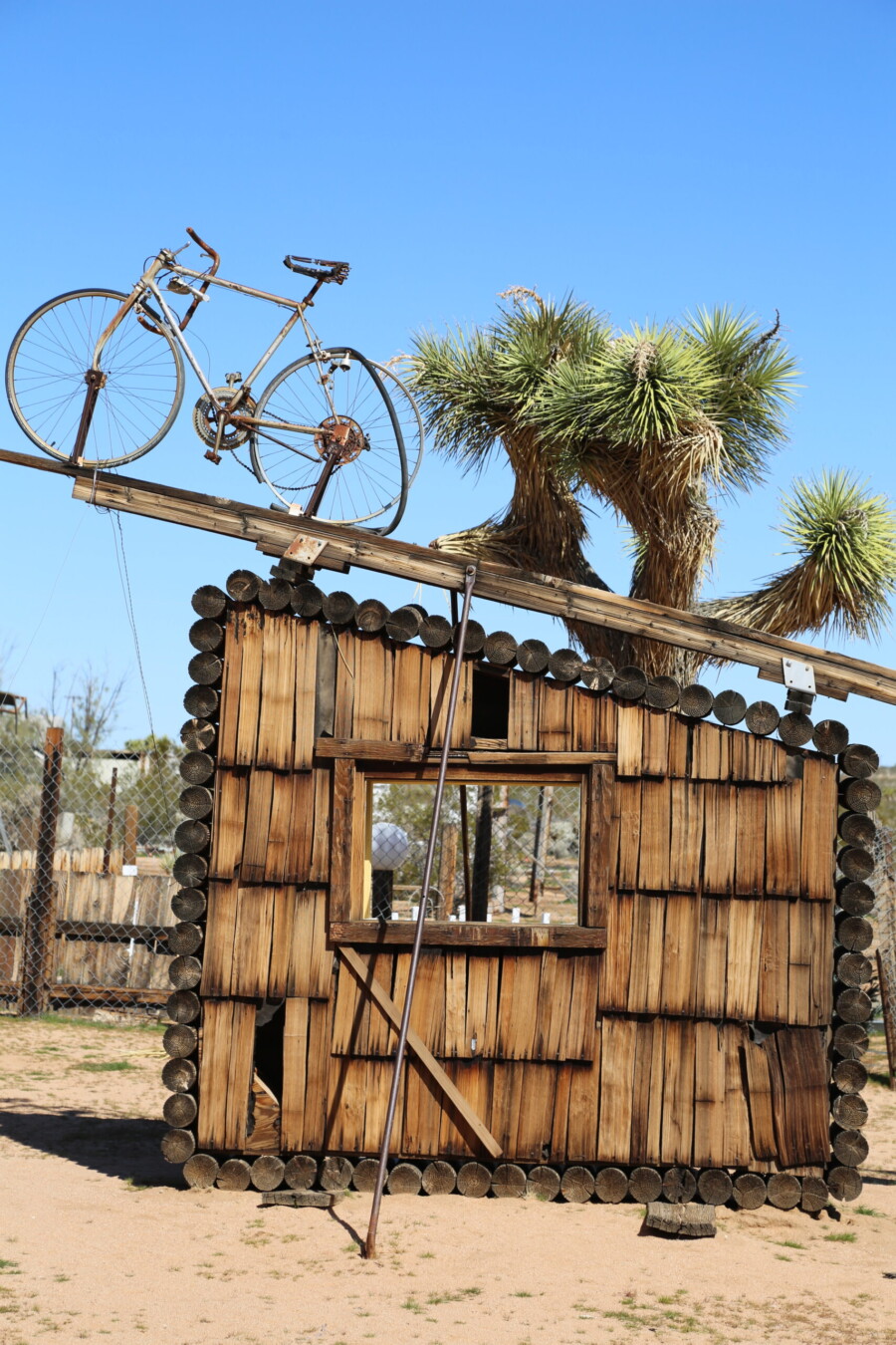 Sculpture installation of a wall with a bicycle balancing on top at the Noah Purifoy Museum of Assemblage Sculpture in Joshua Tree, Califorrnia.